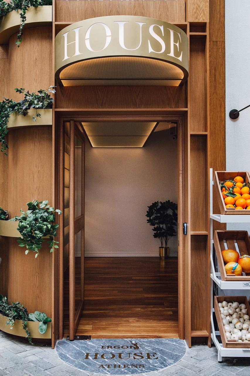 Entrance to ERGON House Athens with brass HOUSE awning, open wooden doorway and fresh produce in wooden crates
