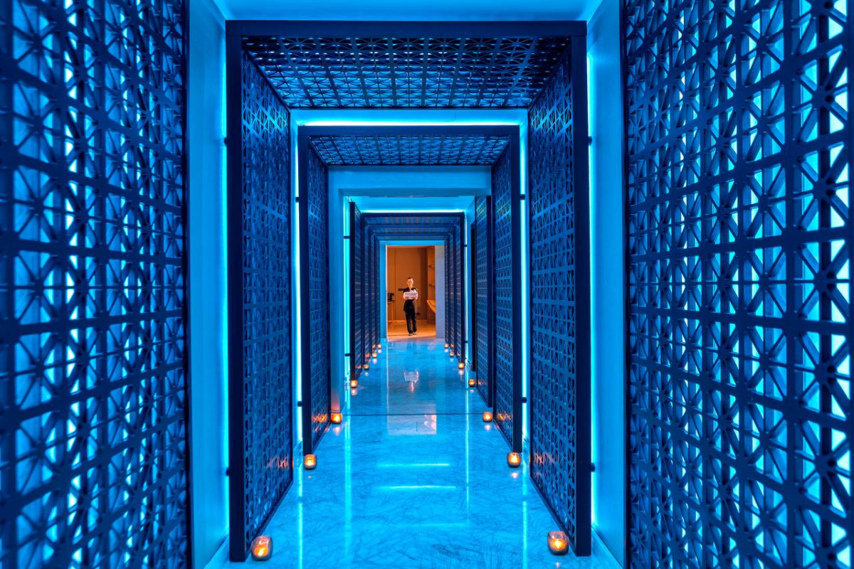 Blue-lit spa corridor at Four Seasons Hotel Limassol with geometric lattice panels and lanterns leading to a warm doorway
