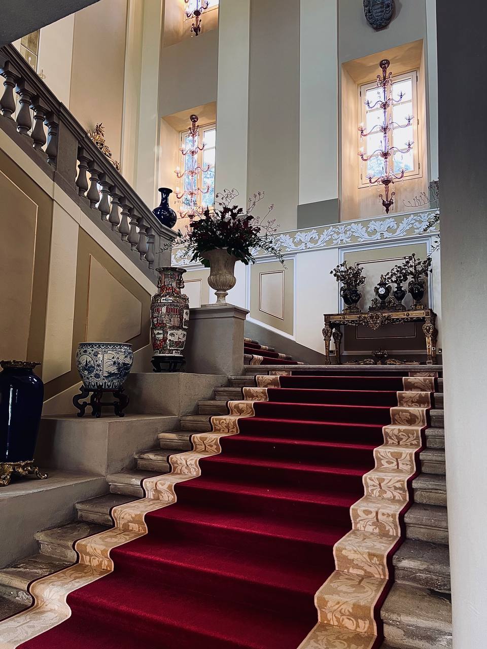 Grand staircase with red carpet and ornate balustrades inside Passalacqua villa