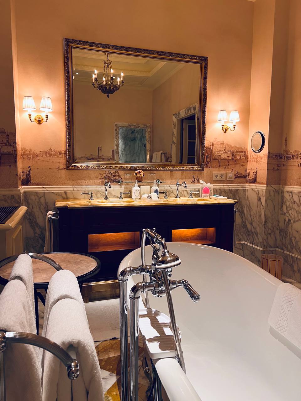 Bathroom vanity with sepia scenic wallpaper and crystal sconces