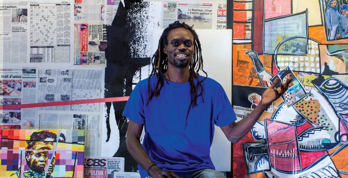 Barkinado BOCOUM in his studio holding a collage piece, surrounded by newspaper and mixed-media works
