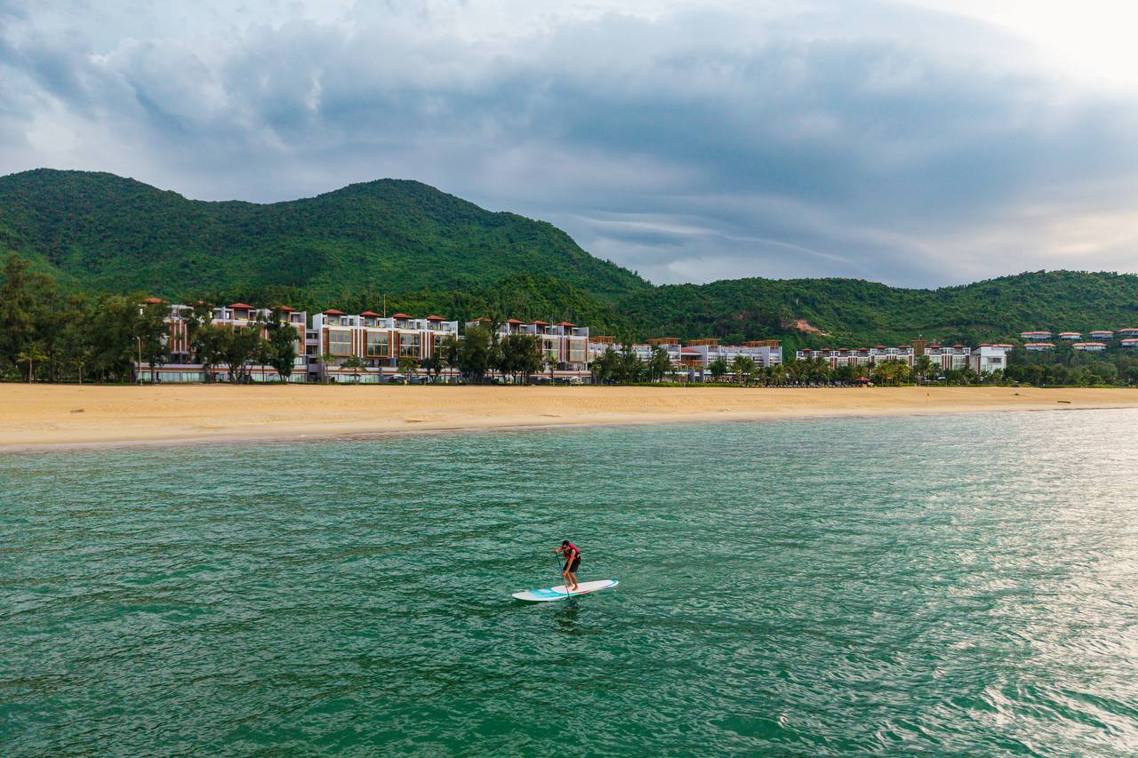 Paddleboarder on calm turquoise water with resort and mountains behind