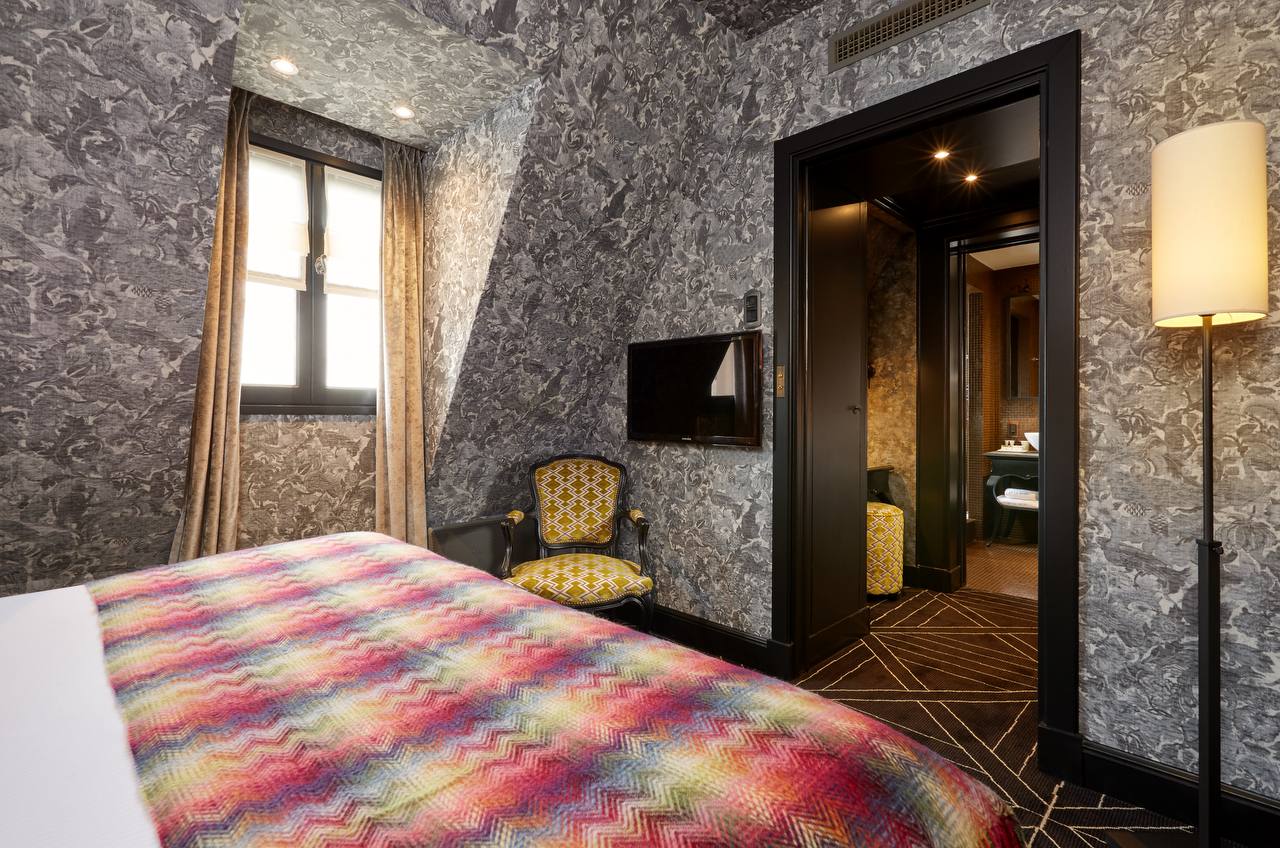 Suite with vibrant coverlet and dark toile wallpaper at Pavillon de la Reine