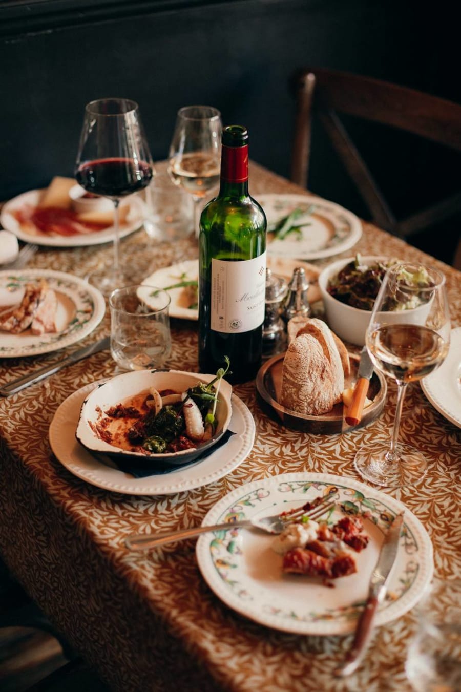 Dinner table with wine, bread and shared plates on gold tablecloth at Mamie Good