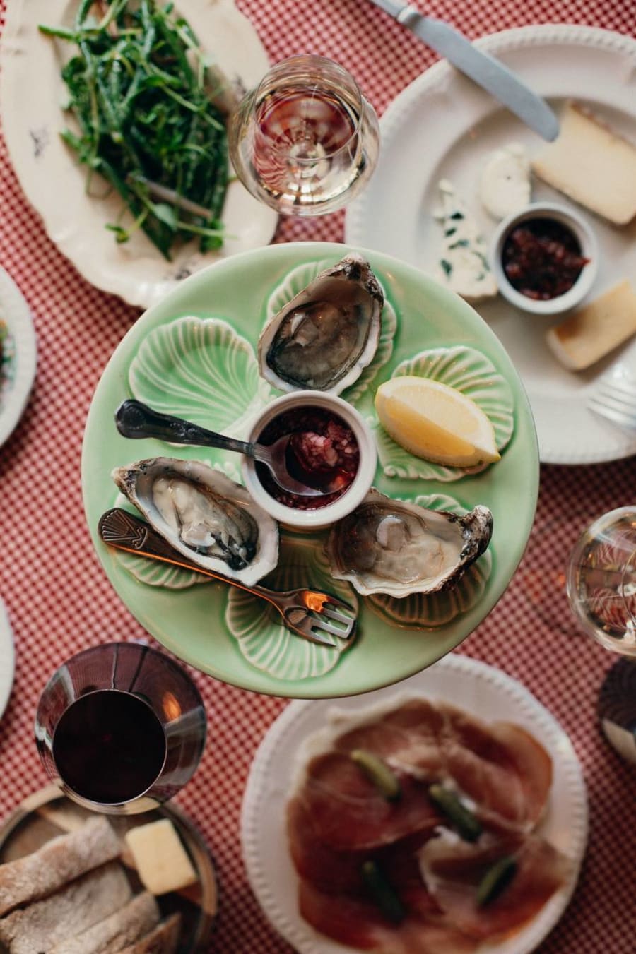 Overhead view of oysters, cheese, charcuterie and wine on checkered tablecloth at Mamie Good