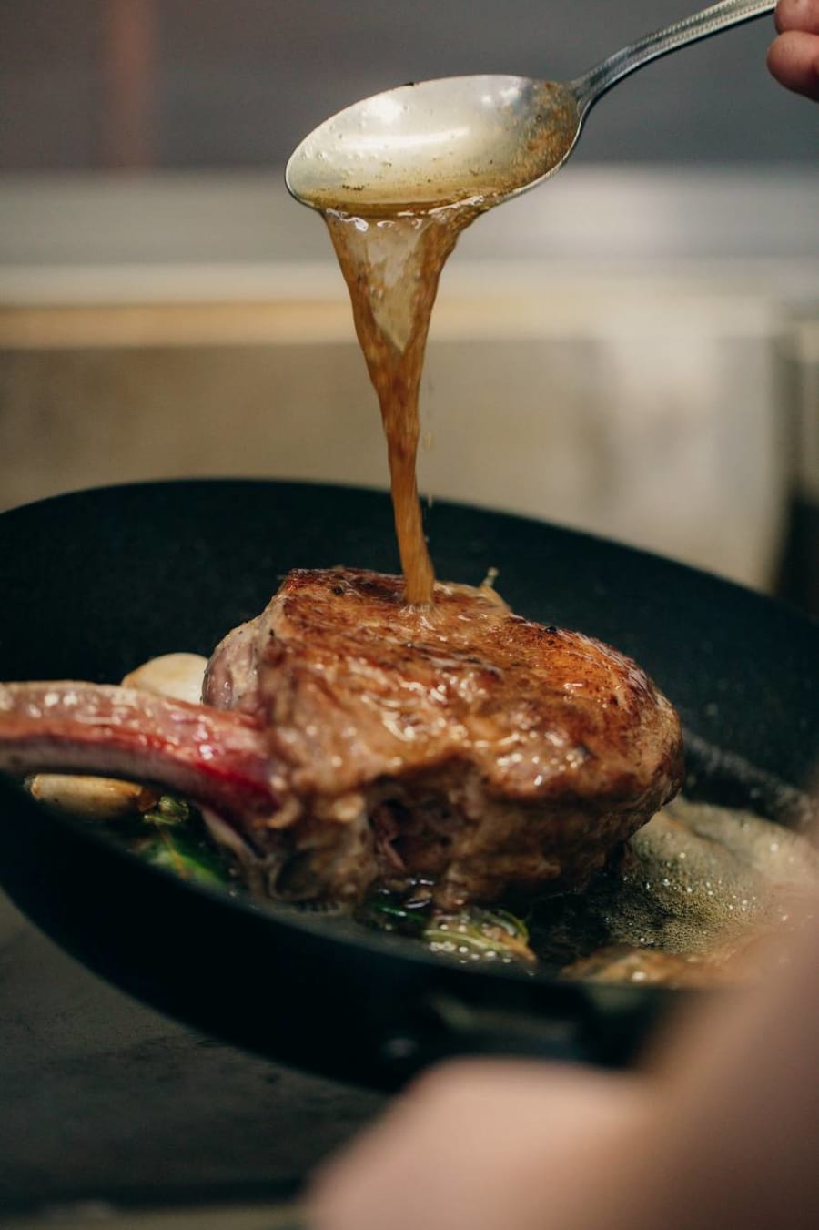 Searing steak in a black skillet with garlic and herbs at Mamie Good