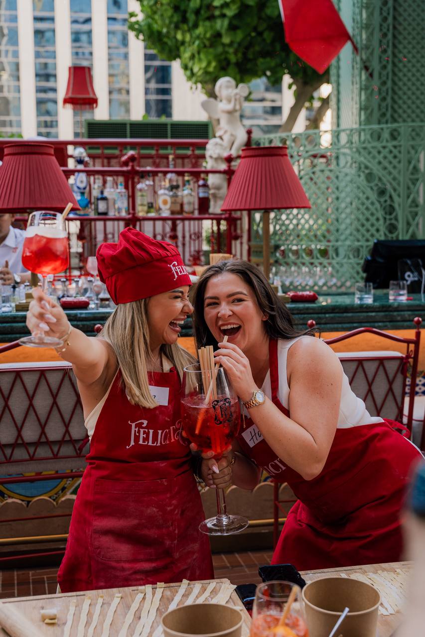 Women in red Felicità aprons enjoy cocktails at an outdoor cooking event