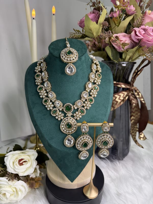 A luxurious dark green Kundan necklace displayed on a bust with matching earrings.
