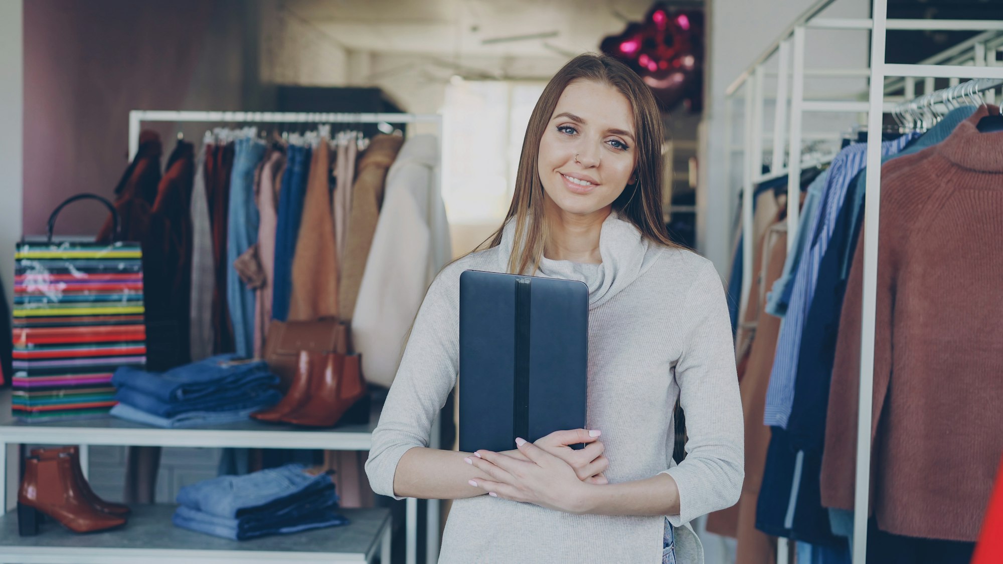 Chủ shop thời trang nhỏ cầm máy tính bảng đứng trong cửa hàng quần áo