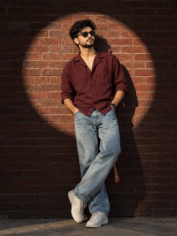 Young South Asian Man In Maroon Shirt Against Brick Wall