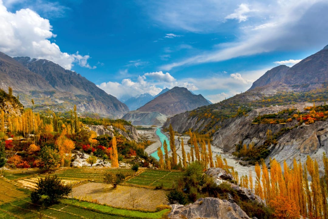 Autumn in Gilgit-Baltistan with golden trees, colorful fall foliage, traditional Hunza village houses, and snow-capped Karakoram mountains.