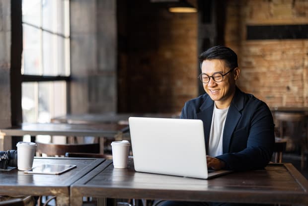 a smiling man typing on a laptop 