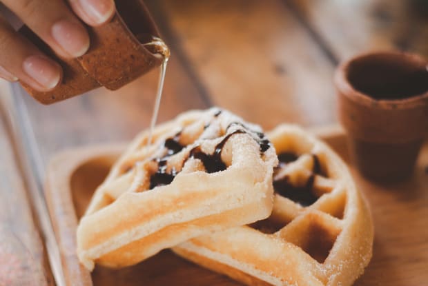 a person pouring honey onto some waffles