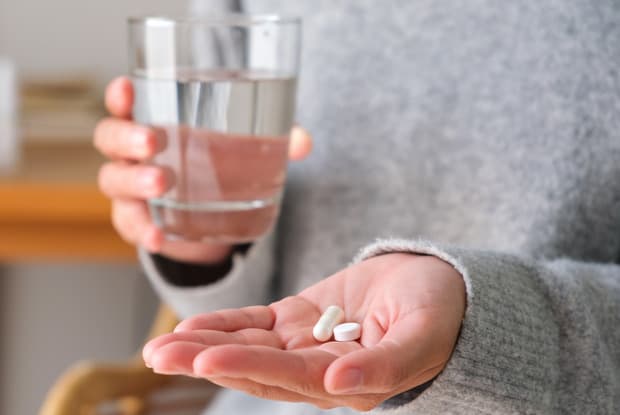 a person holding a glass of water and a pain reliever