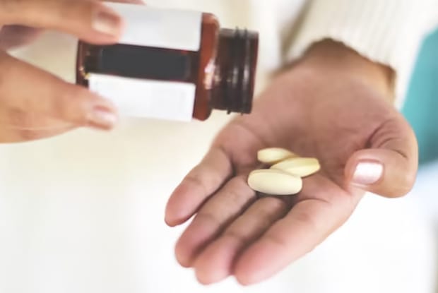 a person pouring several tablets into their hand