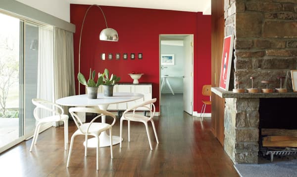 Dining area with back wall painted in Caliente (2018 colour of the year by Benjamin Moore). Brick wall on one side and white plain furniture.