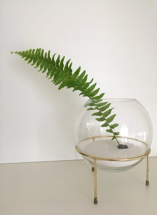 Minimal sculptural vase with a single-leaf arrangement.