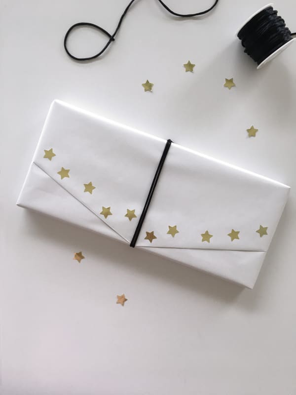 Gift wrapped in ordinary white paper and decorated with a ribbon and golden paper stars as an example of sustainable gift wrapping.