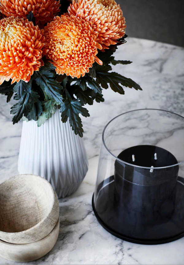 Close-up of a styling with a black candle, wooden bowl and bold orange flowers.