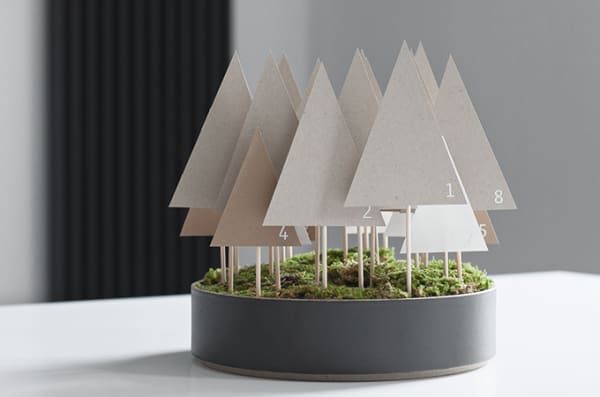 Advent calendar made of paper trees mounted on a wooden stick and tucked in a container onto a moss base.