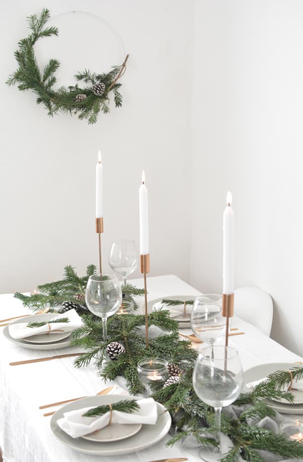 Total white festive table setting with greens and tall candles as a centrepiece.