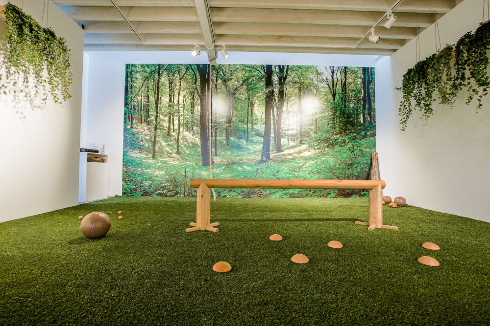 Another view of a biophilic gym. The overall feel is to be immersed in nature, and is achieved with real plants and nature-inspired finishes like a mural depicting a forest and a grass-like carpet.<span class="sr-only"> (opened in a new window/tab)</span>