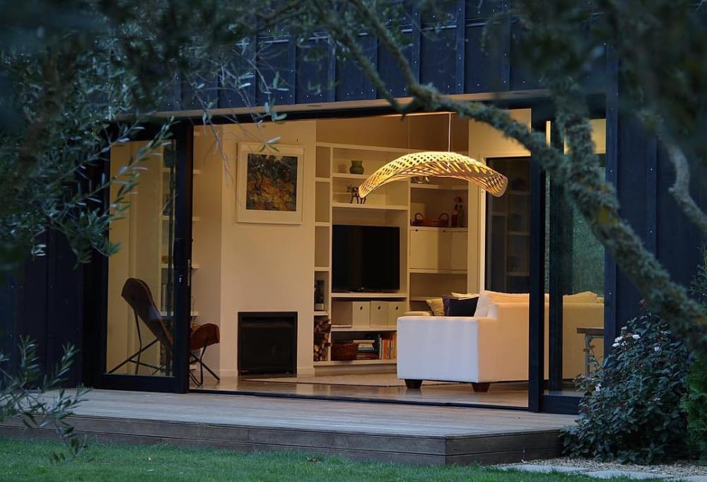 Shoot of a living room over branches highlighting a sinuous light fixture.<span class="sr-only"> (opened in a new window/tab)</span>