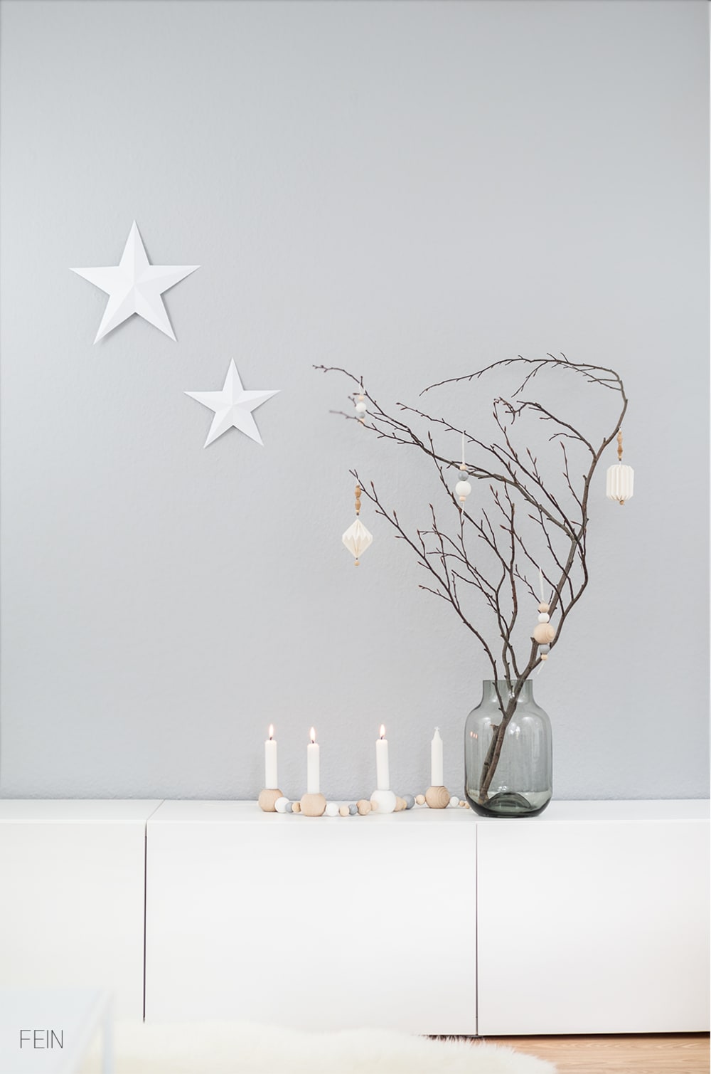 Branch decorated with white ornaments on a light grey wall background.<span class="sr-only"> (opened in a new window/tab)</span>