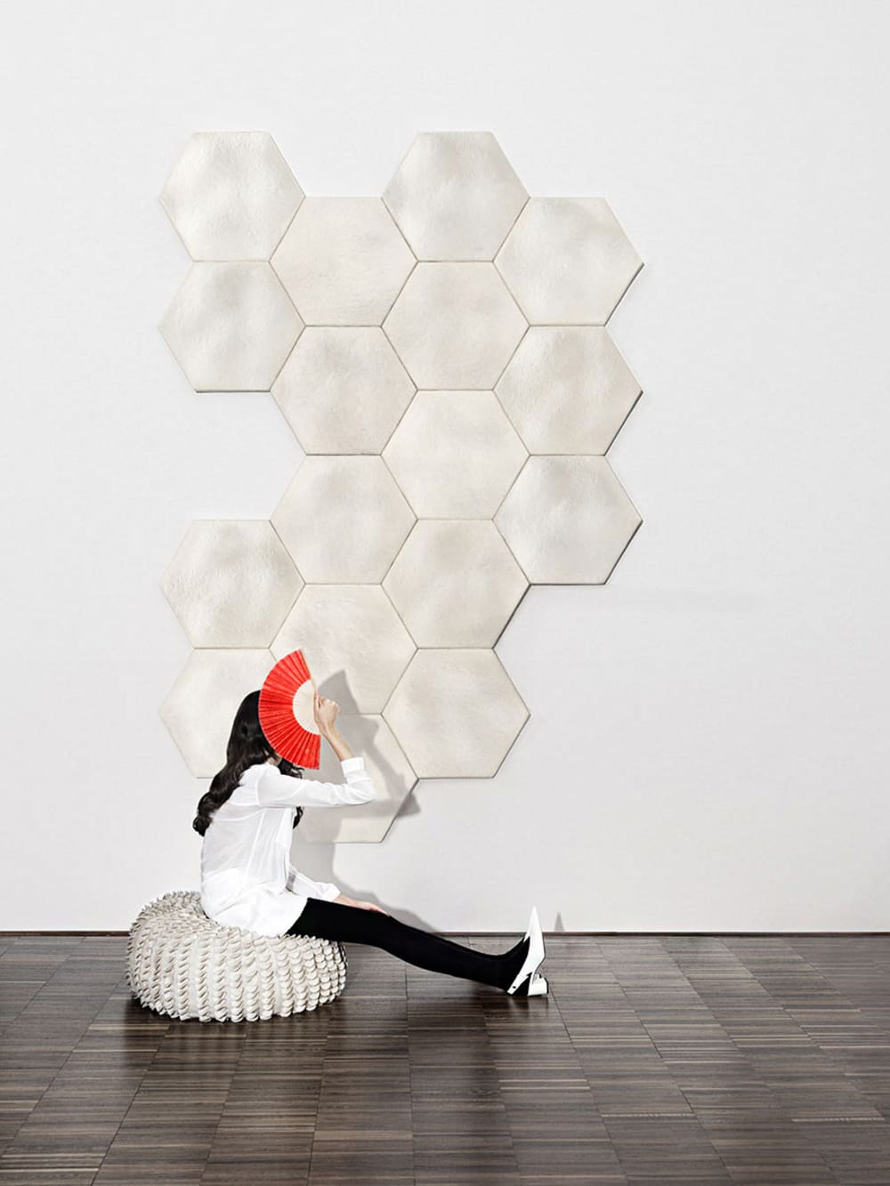 Girl sitting in front of a wall decorated with acoustic tiles made of mushroom mycelium.<span class="sr-only"> (opened in a new window/tab)</span>