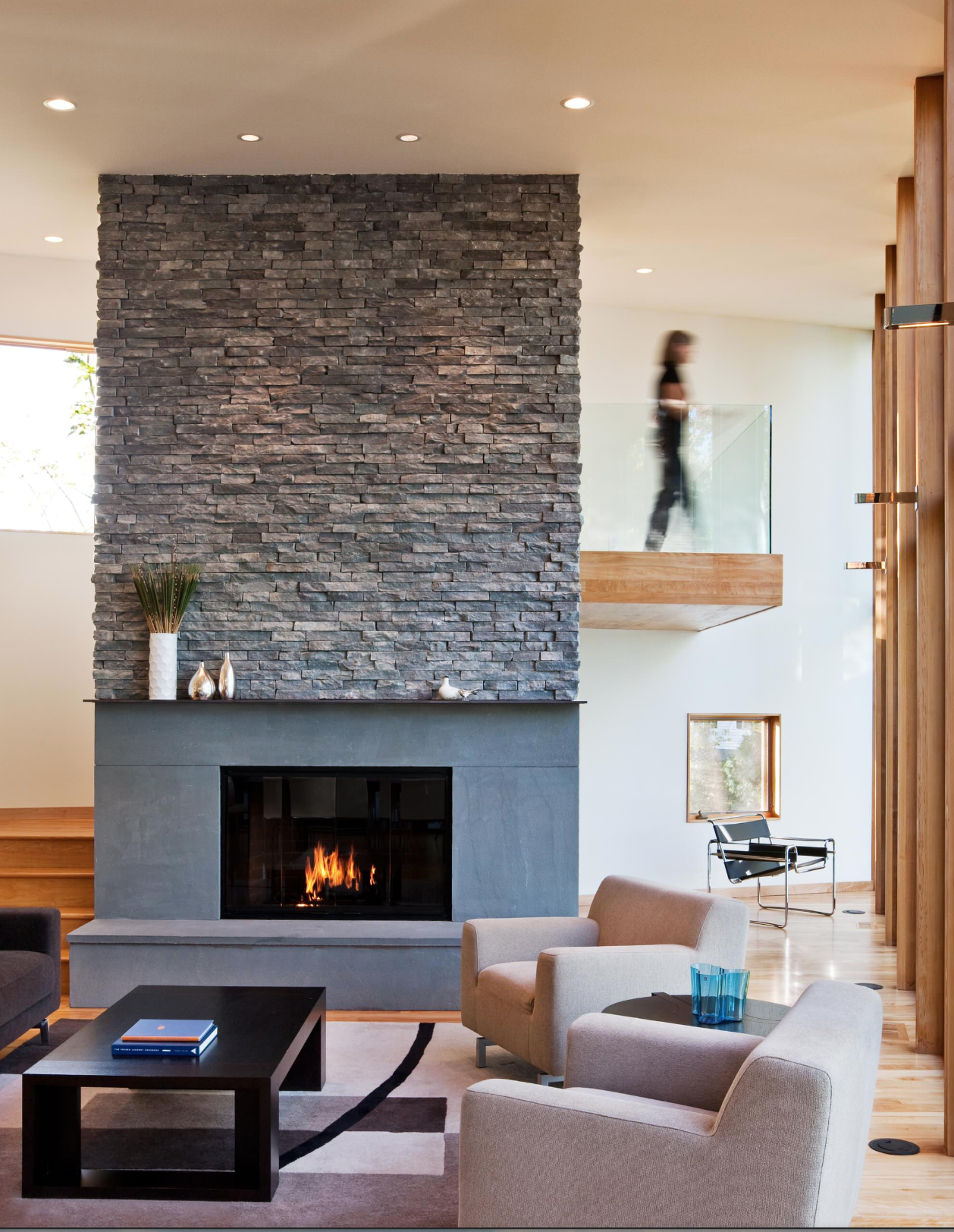A contemporary living room with huge fireplace cladded in dark stone.