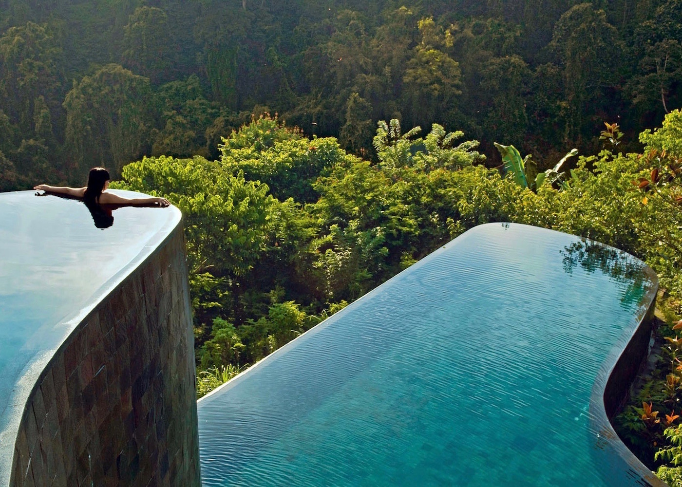 A terraced infinity pool that seems to go right into the forest with a woman on the edge.