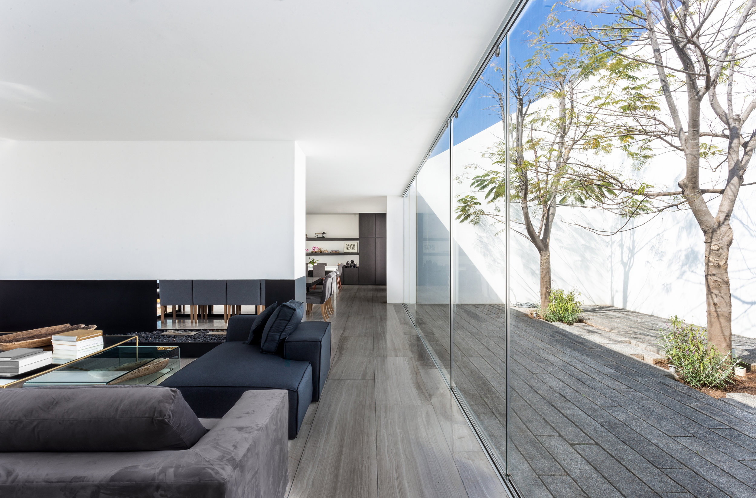 Big indoor-outdoor living room with fully glazed wall looking into trees.