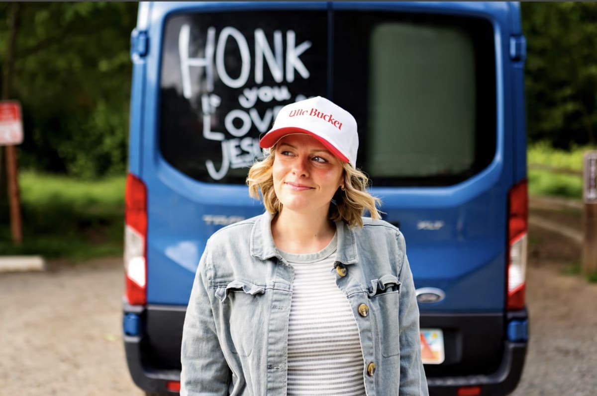 Amy O'Neal, founder of Belle Bucket, standing behind the O'Neal mobile, her family's big blue Ford Transit van, with Honk If You Love Jesus written on the back window