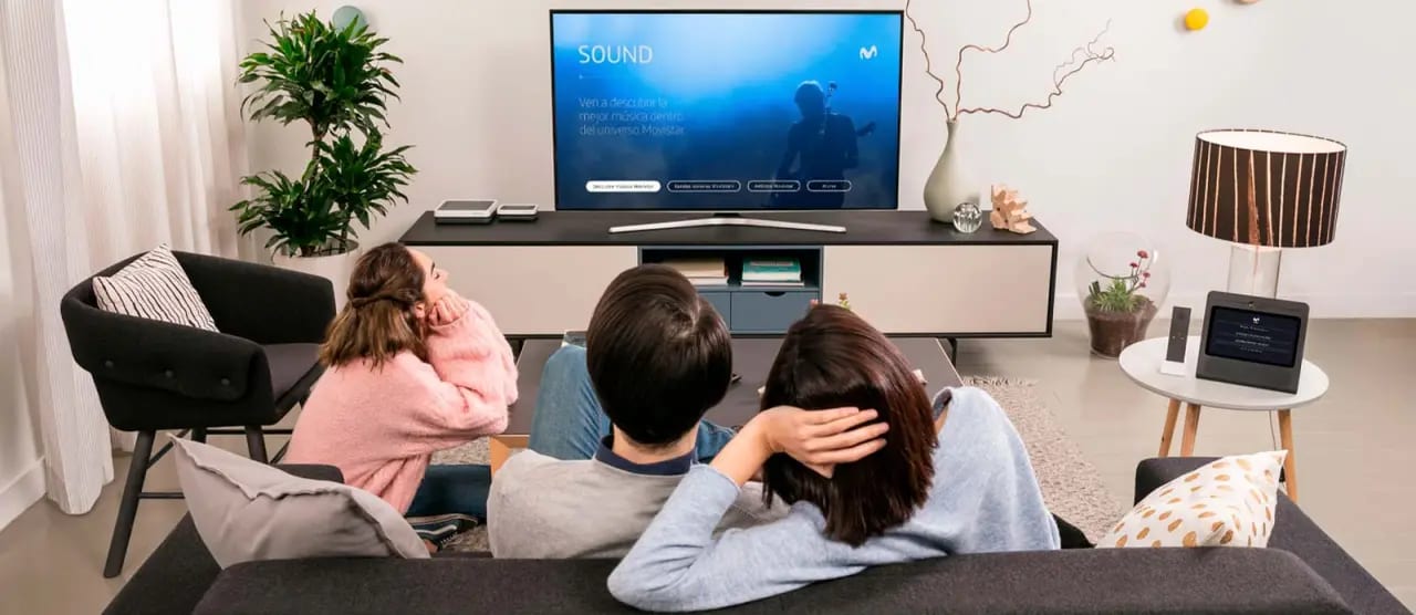 Sala com app da Movistar na TV e dispositivo Movistar Home sobre a mesa.
