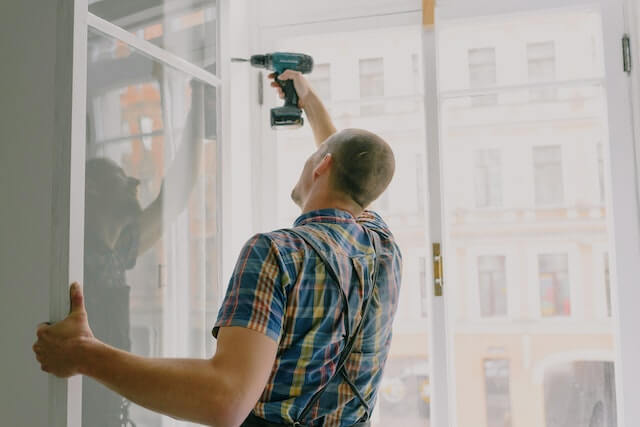 handyman installing window frame with drill inhouse