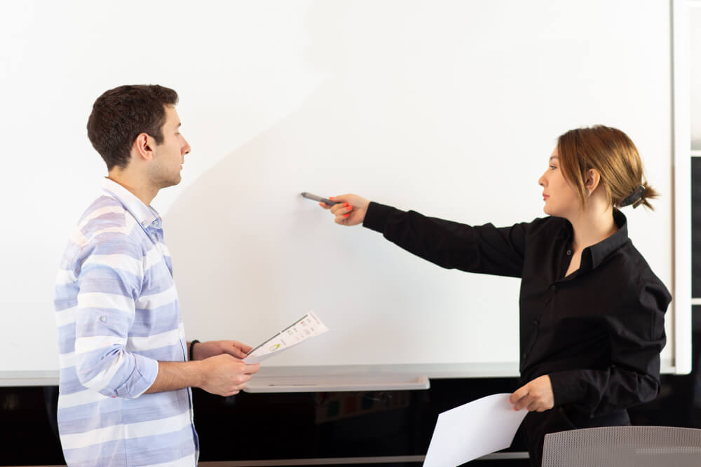 A front view young attractive businesswoman in black shirt along with young man discussing graphics on the desk