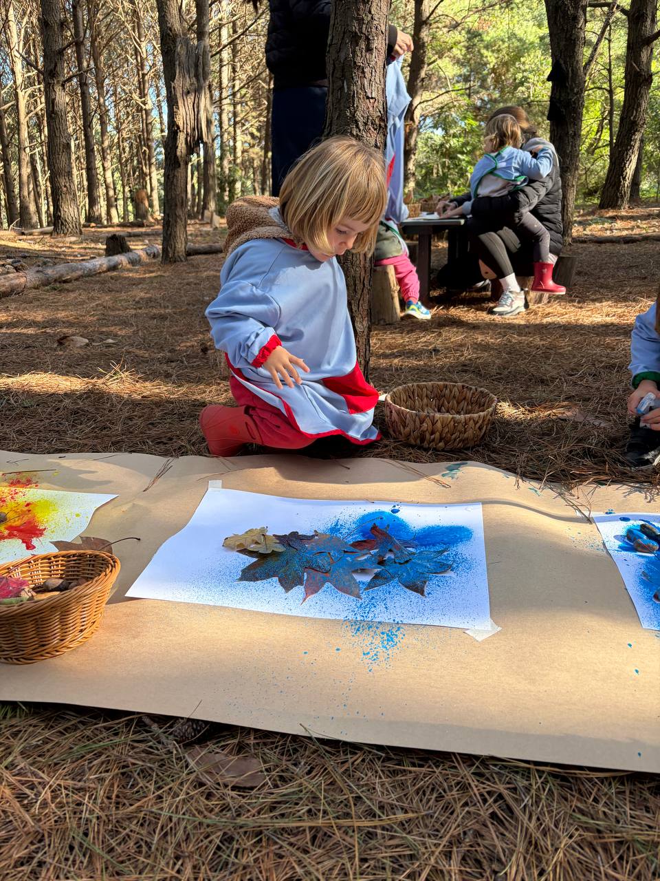 Una niña observa una obra con hojas y pintura azul en el bosque