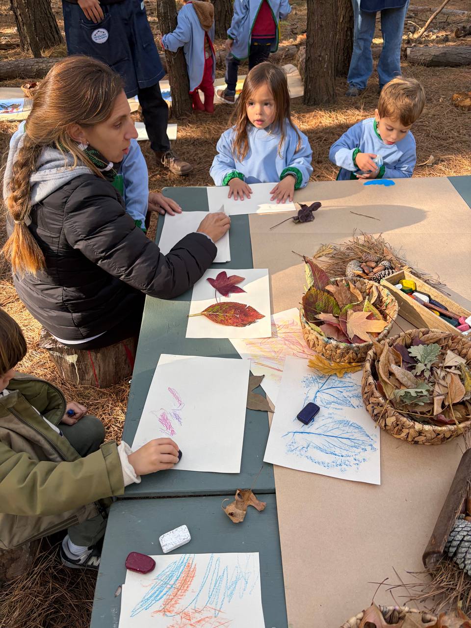 Niños dibujando con hojas, colores y materiales naturales sobre una mesa