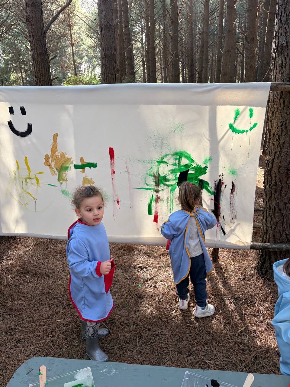 Niños pintando un gran lienzo colgado entre los arboles