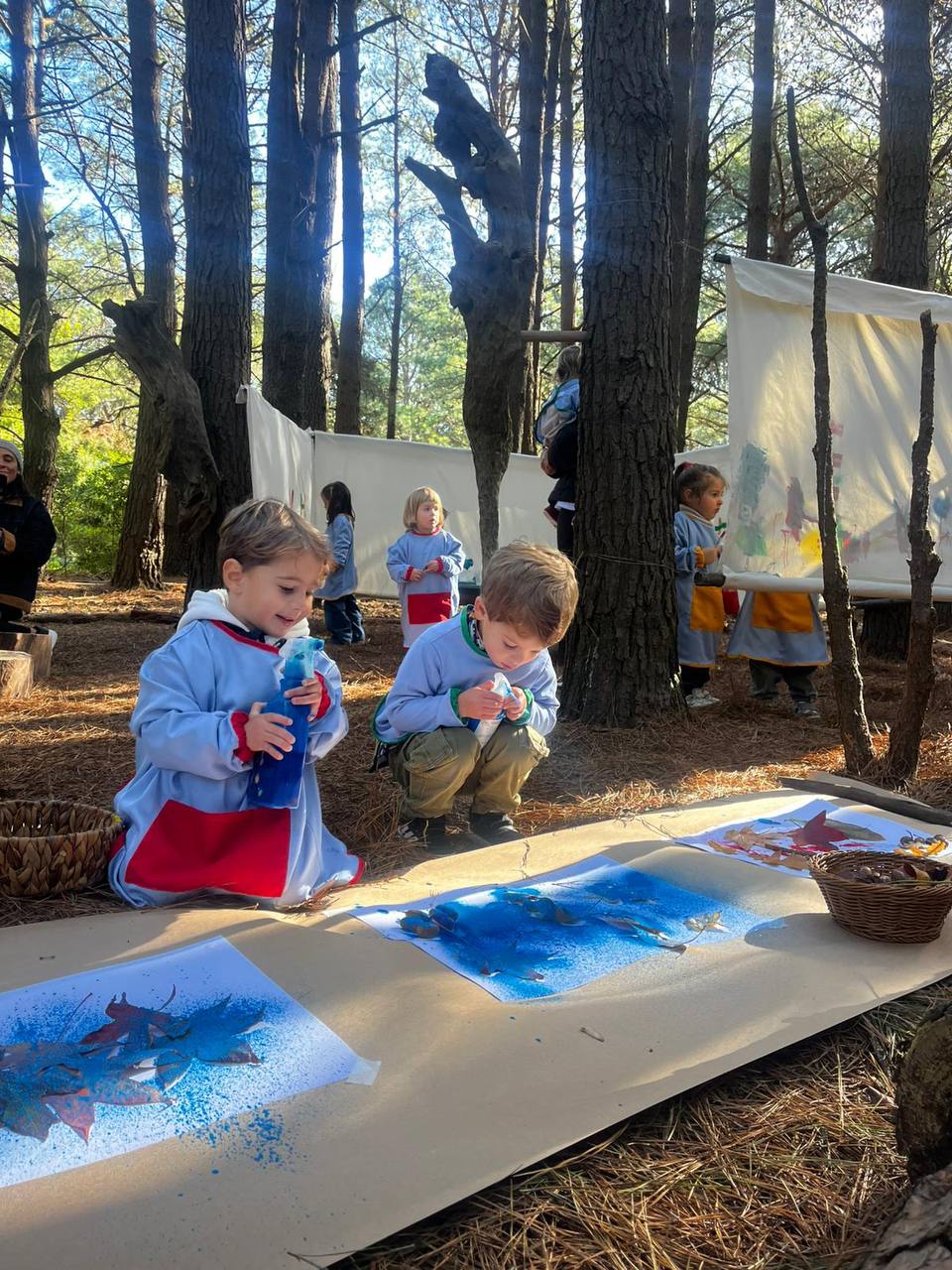 Ninos creando obras con colores y hojas en mesas al aire libre