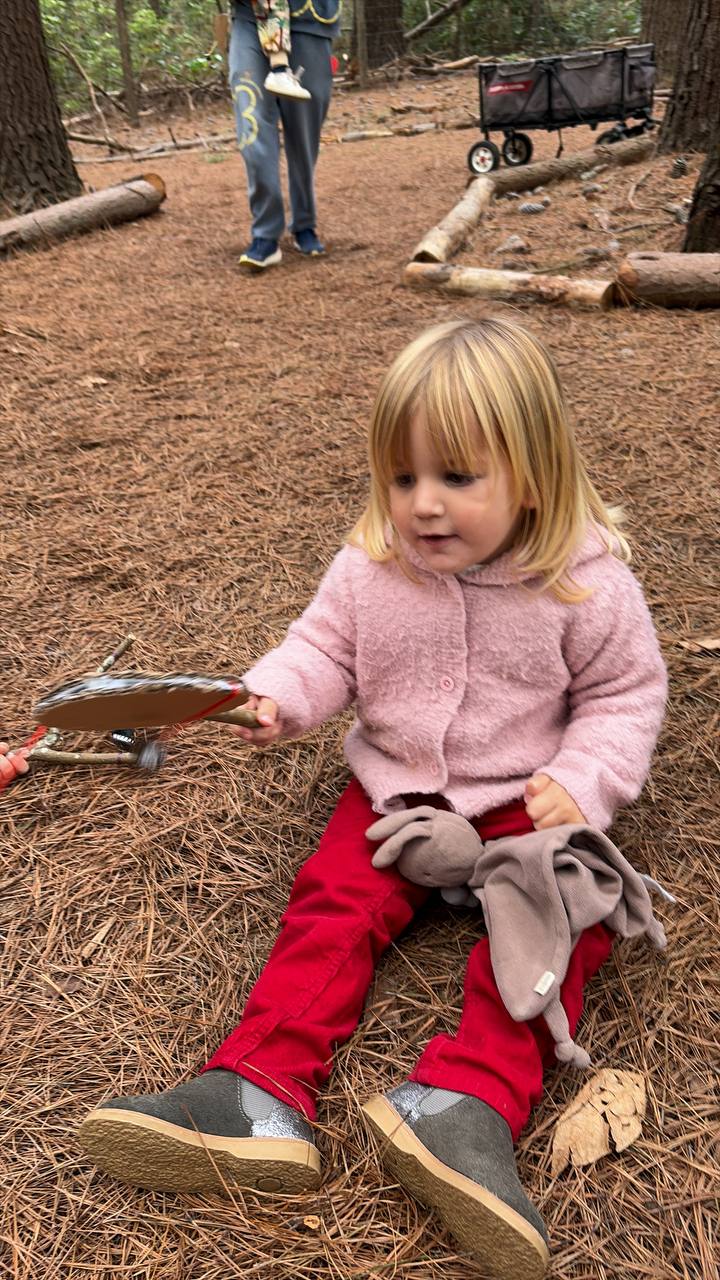 Niña explorando un instrumento de mano en el suelo del bosque