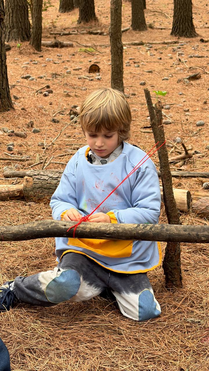 Niño concentrado atando y construyendo un instrumento con ramas