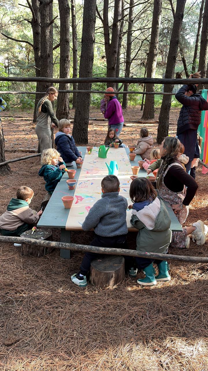 Ninos pintando macetas en una mesa larga dentro del bosque