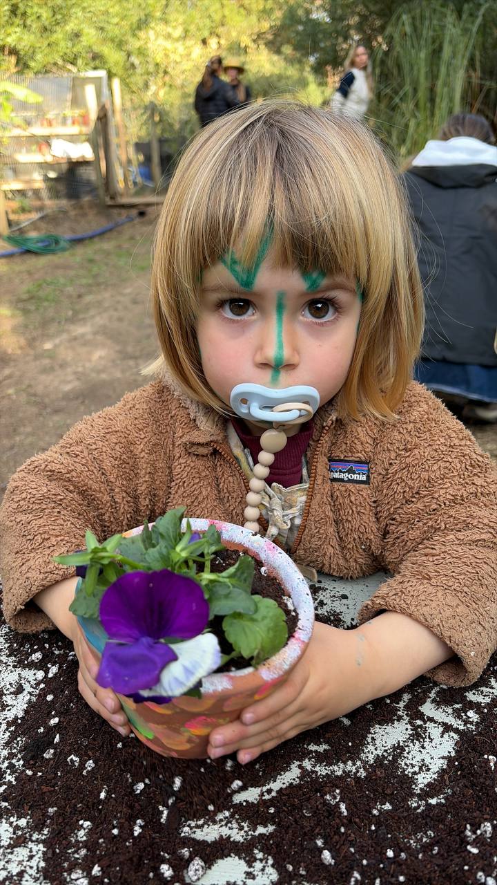 Nina sosteniendo una maceta con una flor violeta recien plantada