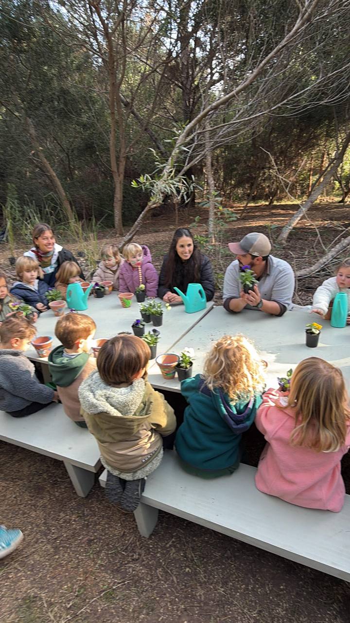 Ninos y familias reunidos en una mesa del bosque con plantas y regaderas