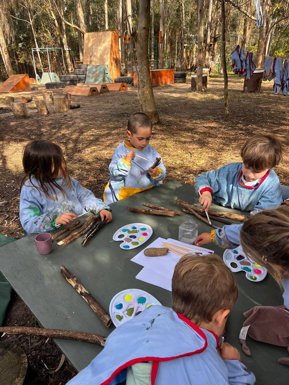 Niños pintando palitos en una mesa del bosque