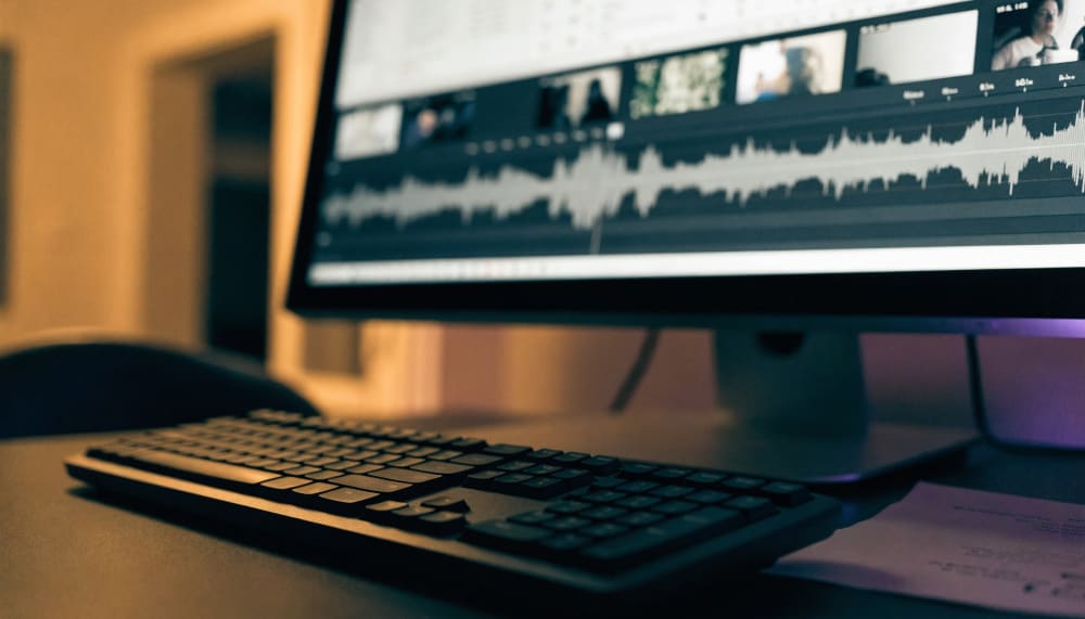 An editing timeline on a desktop monitor with six short video clips laid end to end, a separate audio track running bene