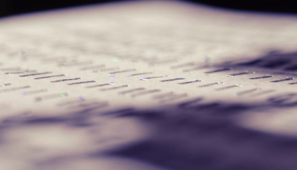 Close-up of a printed page of prose, most letters in soft focus, a scattering of individual letters catching a faint iri
