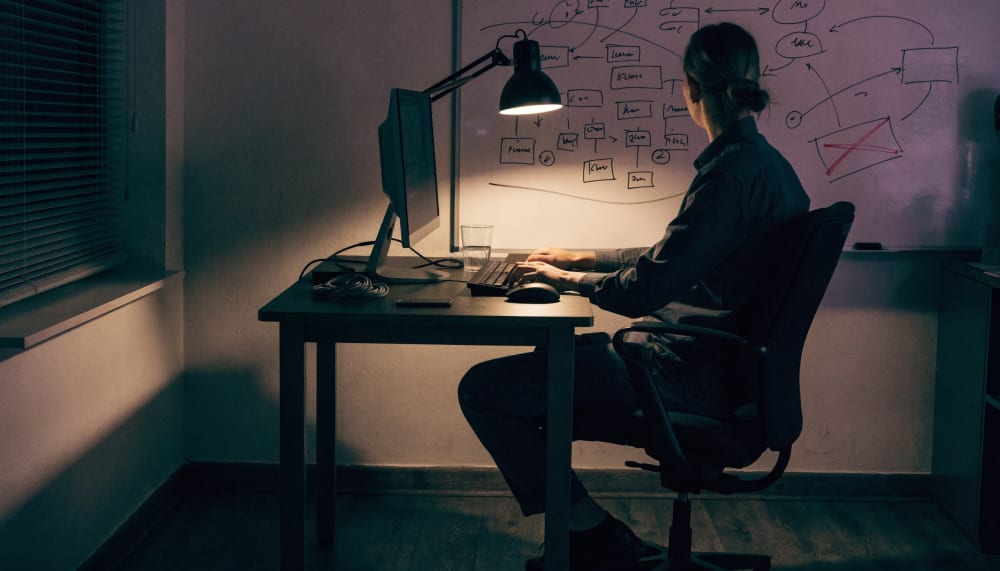 A developer's desk at night, a whiteboard behind it covered in a hand drawn agent orchestration diagram with boxes and a