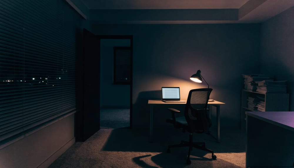 An empty small office at night, a single laptop left open on a desk showing a spreadsheet, warm desk lamp light, nobody